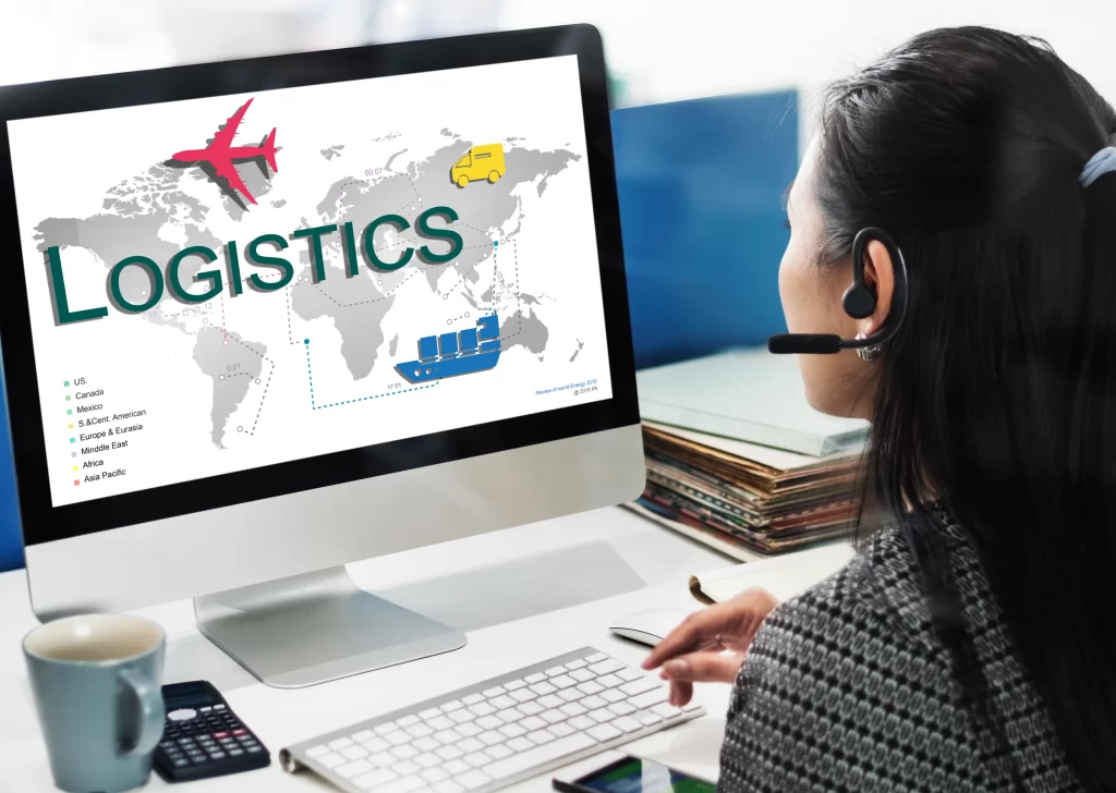 Person wearing a headset looking at a computer monitor displaying a world map and logistics graphics (airplane, ship, and routes).