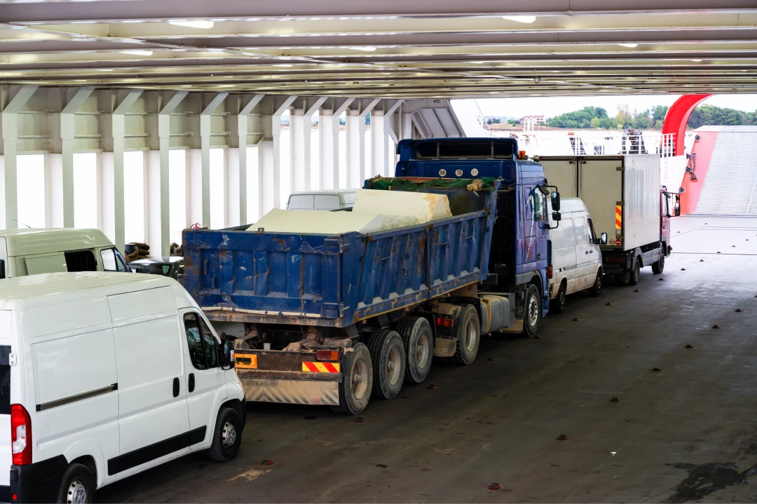 Line of white delivery vans and a blue dump truck inside a long covered loading dock at a logistics terminal.
