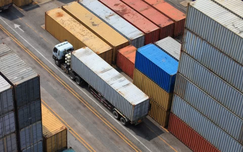Aerial view of stacked colorful shipping containers in a yard, with a small truck at the left side.